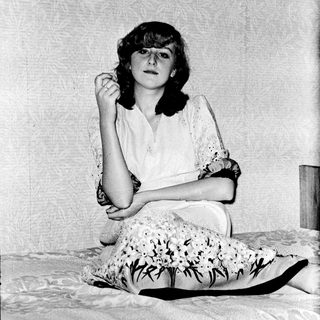 A woman sitting on a bed, adjusting her glasses.