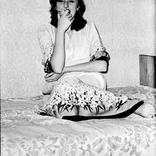 A woman sitting on a bed, holding a cigarette.