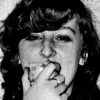 A woman sitting on a bed, holding a cigarette.