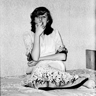 A woman sitting on a bed, holding a cigarette.