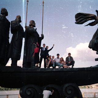 Group posing on historic ship statue.
