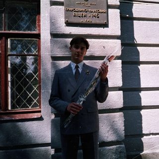 Young man in school uniform holding saxophone outside building.