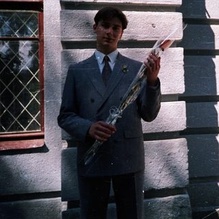 Young man in school uniform holding saxophone outside building.