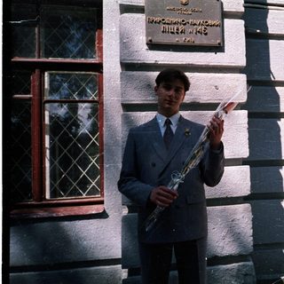 Young man in school uniform holding saxophone outside building.