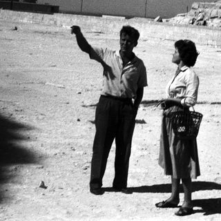 Two people pointing at ancient pyramid ruins.