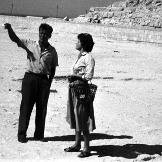 Two people pointing at ancient pyramid ruins.