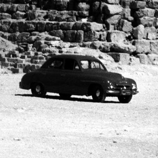 Ancient pyramid with vintage car in desert.