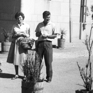 Two people holding potted plants outside a building.