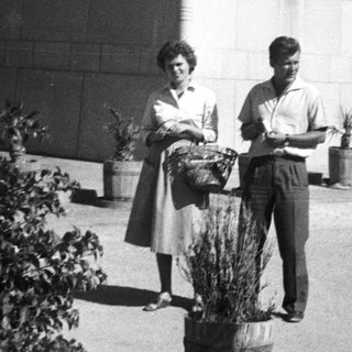 Two people holding potted plants outside a building.