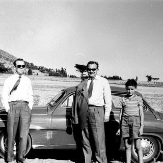 Three men and a child posing by vintage car in rural outdoor setting.