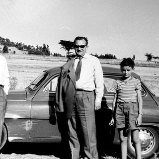 Three men and a child posing by vintage car in rural outdoor setting.