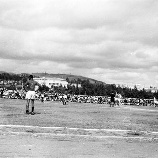 Baseball game with pitcher on mound, spectators in stands.