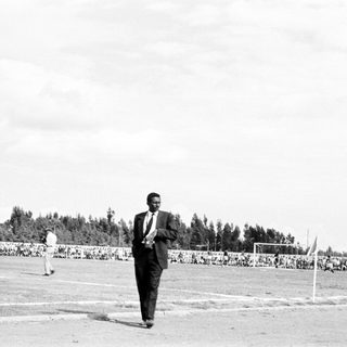 Man in suit inspects sports field with spectators.