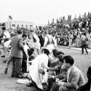 People gathered outdoors, some standing, some sitting, during what appears to be a public event or gathering.