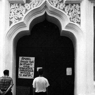 People standing near a closed door with a protest sign in Cyrillic.