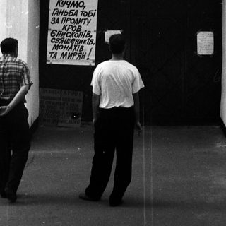 People standing near a closed door with a protest sign in Cyrillic.