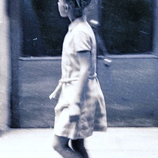A girl in a dress walks quickly outdoors.