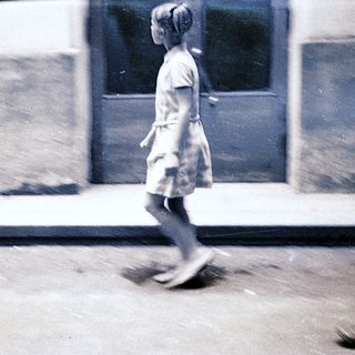 A girl in a dress walks quickly outdoors.