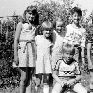 Five children posing happily outdoors in summer clothes.