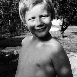 Shirtless boy smiling outdoors in black-and-white.