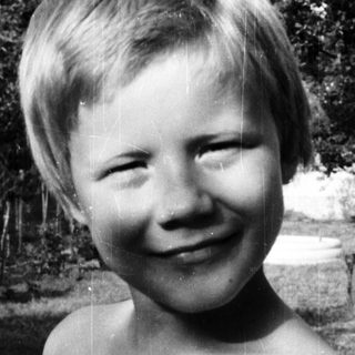 Shirtless boy smiling outdoors in black-and-white.