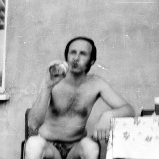 Shirtless man eating indoors, vintage photo.