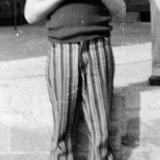 Two people standing outdoors near a building. Woman holding a bag, boy holding a booklet.