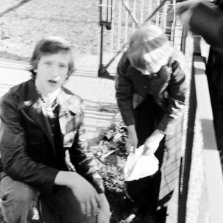 Two people near a bridge, one sitting, one bending.