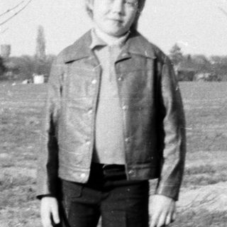 Young boy standing outdoors in a field.
