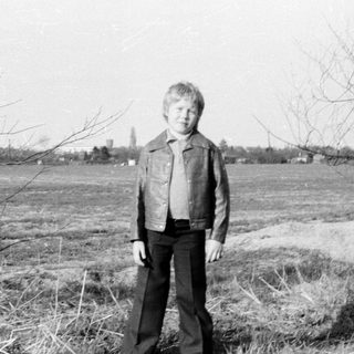 Young boy standing outdoors in a field.