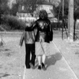 Two people walking a dog on a paved path.