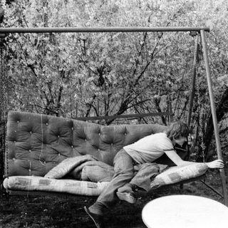 Person lying on a suspended mattress swing outdoors.