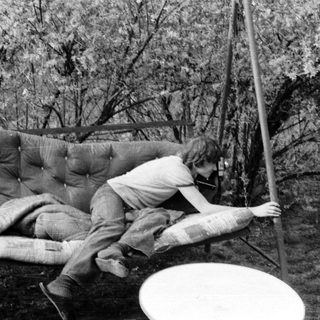 Person lying on a suspended mattress swing outdoors.