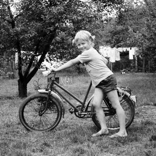 Young child posing joyfully on a bicycle outdoors.