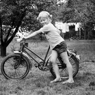 Young child posing joyfully on a bicycle outdoors.