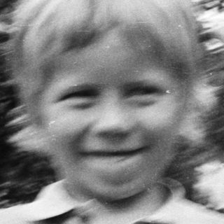 Smiling young child outdoors in blurry black-and-white photo.