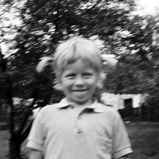 Smiling young child outdoors in blurry black-and-white photo.