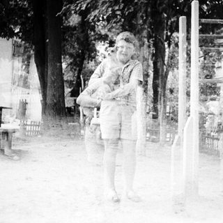 A person holding a child outdoors near fenced area.