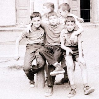 Five boys hugging in an urban courtyard.