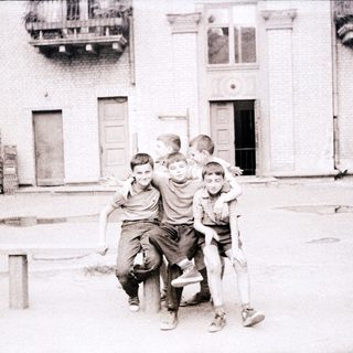 Five boys hugging in an urban courtyard.