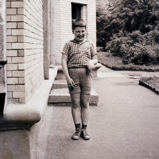 Young boy smiling outside a building holding a book.