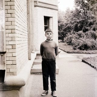 Young boy standing outdoors near brick building.
