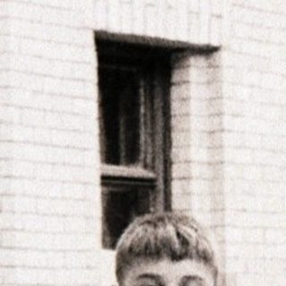 Young boy standing outdoors near brick building.