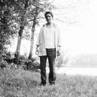 Person standing alone in misty outdoor field near water.