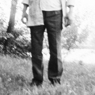 Person standing alone in misty outdoor field near water.