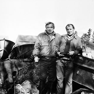 Two men standing outdoors near agricultural equipment.
