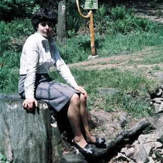 Woman sitting on rock near hiking trail signs.