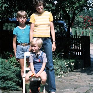 Three children posing outdoors in 1980s-style clothing.