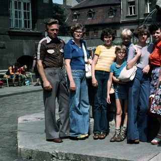 Group of eight people posing together outdoors in 1970s-style clothing.