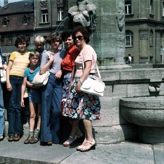 Group of eight people posing together outdoors in 1970s-style clothing.